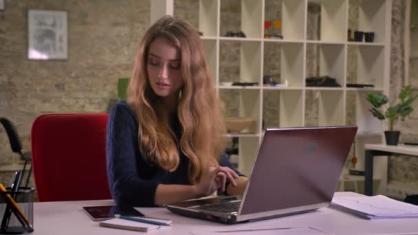 Portret van drukke blonde Kaukasische zakenvrouw werken met laptop in kantoor ontvangt kennisgeving op Tablet PC. - Video