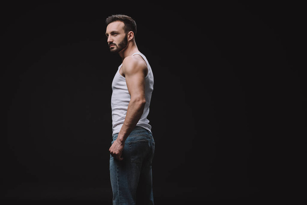 handsome man posing in white singlet and jeans isolated on black - 写真・画像