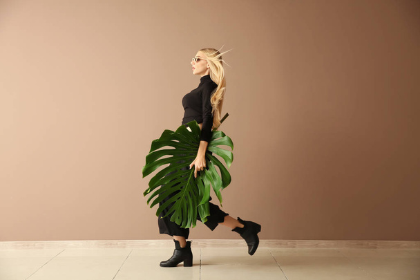 Beautiful woman with green tropical leaf near color wall - Foto, Imagem