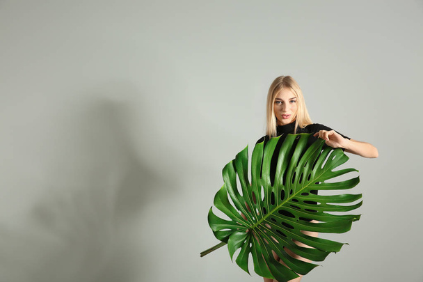 Portrait of beautiful woman with green tropical leaf on light background - Photo, image
