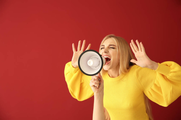 Emotionele jonge vrouw met megafoon op kleur achtergrond - Foto, afbeelding