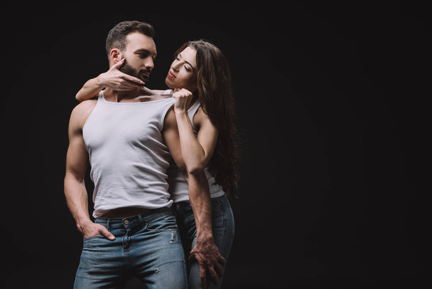 sexy woman hugging and undressing man in white singlet isolated on black - Fotografie, Obrázek
