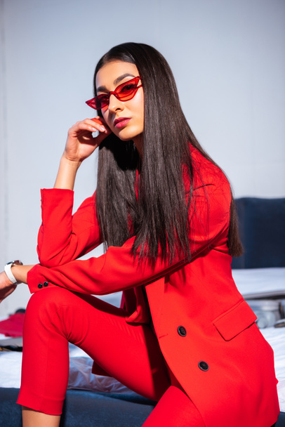 beautiful young woman in stylish red suit and sunglasses sitting and looking at camera - Photo, Image