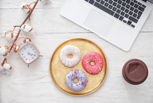 Composition with tasty doughnuts and laptop on white wooden table - Photo, Image