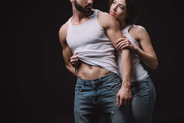 cropped view of girl hugging and undressing man in white singlet isolated on black - Fotografie, Obrázek