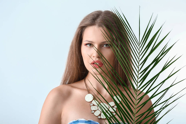 Portrait of beautiful woman with green tropical leaf on light background - Valokuva, kuva