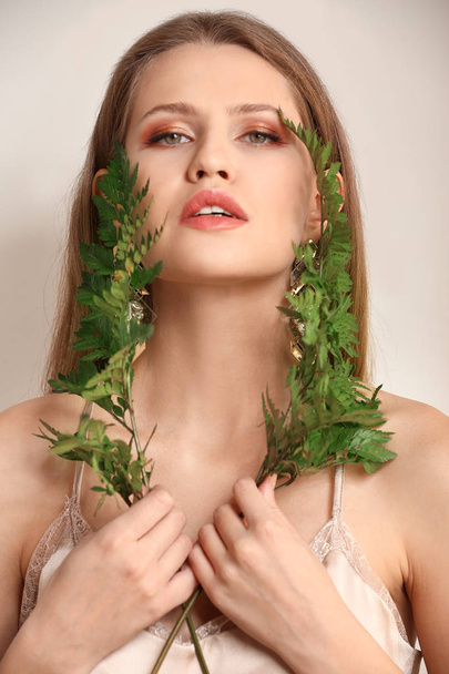 Portret van mooie vrouw met groene fern laat op lichte achtergrond - Foto, afbeelding