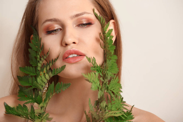 Portrait of beautiful woman with green fern leaves on light background - Photo, Image