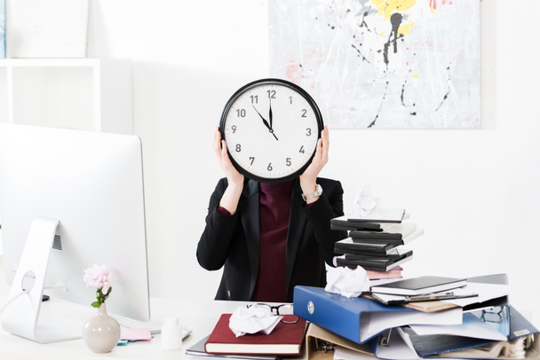 businesswoman covering face with clock in office - Φωτογραφία, εικόνα