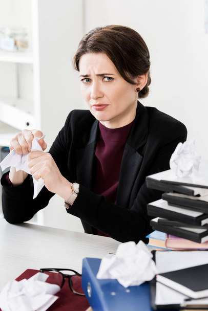 triste atractiva mujer de negocios rasgando papeles y mirando a la cámara en la oficina
 - Foto, Imagen