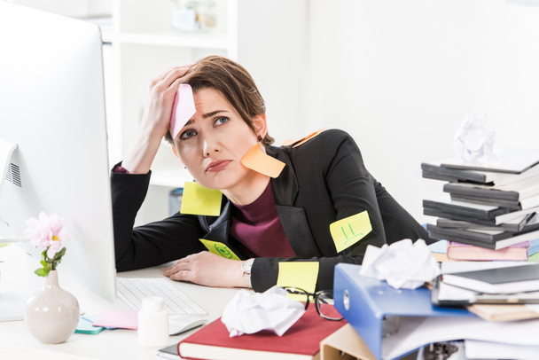 sad attractive businesswoman sitting with stickers on face and clothes in office - Photo, Image