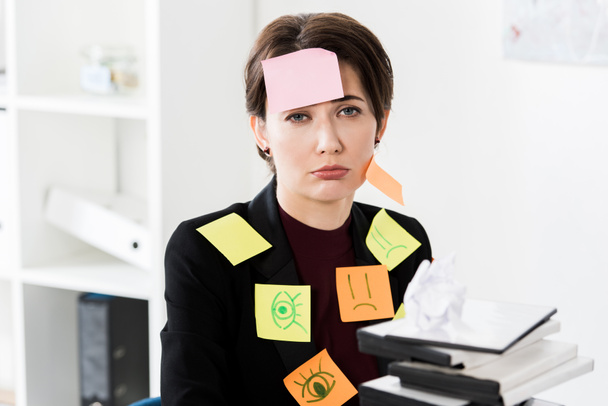 depressief aantrekkelijke zakenvrouw zitten met stickers op gezicht en kleding in kantoor - Foto, afbeelding