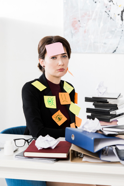 traurig attraktive Geschäftsfrau sitzt mit Aufklebern auf Gesicht und Kleidung im Büro - Foto, Bild