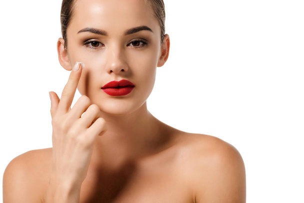 attractive girl with red lips applying cream on face and looking at camera isolated on white - Photo, Image