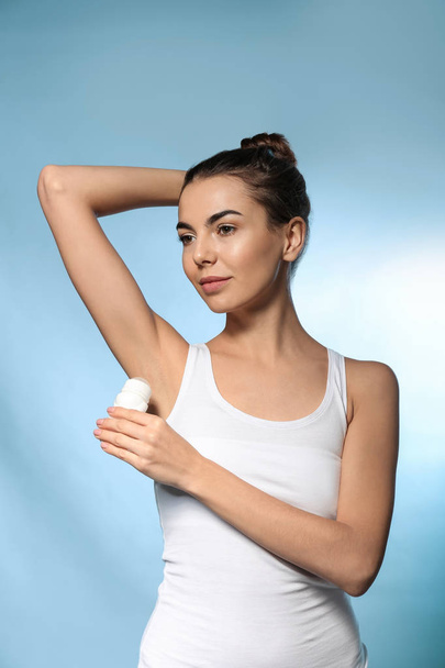 Молодая женщина использует дезодорант на цветном фоне
 - Фото, изображение