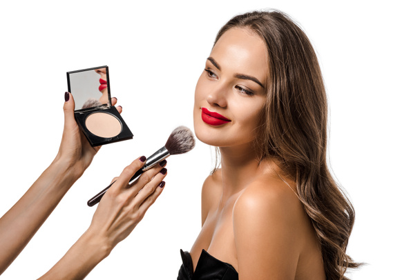 abgeschnittene Ansicht einer Frau, die Puder mit Kosmetikpinsel auf das Gesicht eines attraktiven Mädchens aufträgt, isoliert auf Weiß - Foto, Bild