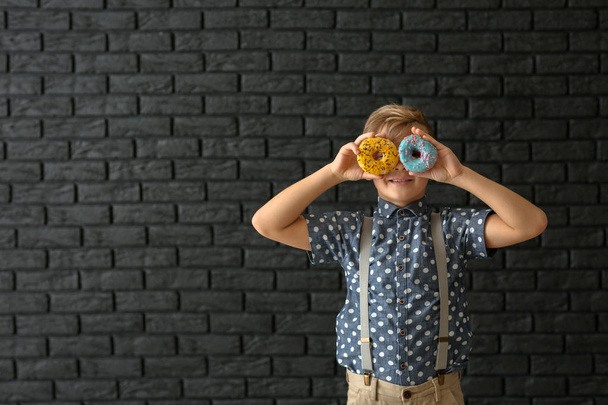 Χαριτωμένο μικρό αγόρι με ντόνατς σε σκούρο φόντο - Φωτογραφία, εικόνα