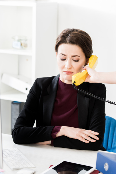 Grijnzende zakenvrouw praten gele stationaire telefonisch in kantoor - Foto, afbeelding