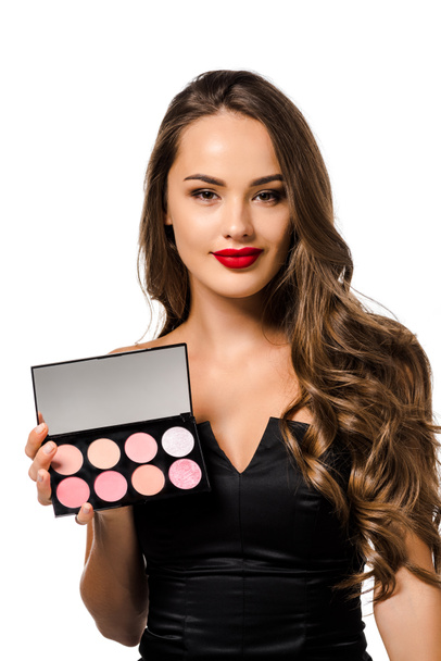 beautiful girl in black dress with red lips holding palette with eyeshadows, looking at camera and smiling isolated on white - Photo, Image