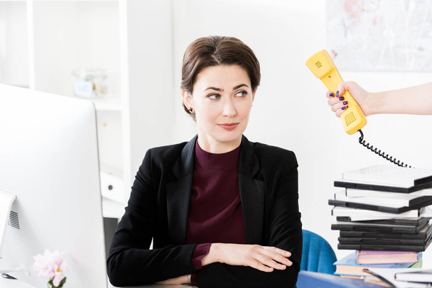 секретарь дает желтый стационарный телефон красивой деловой женщине в офисе
 - Фото, изображение