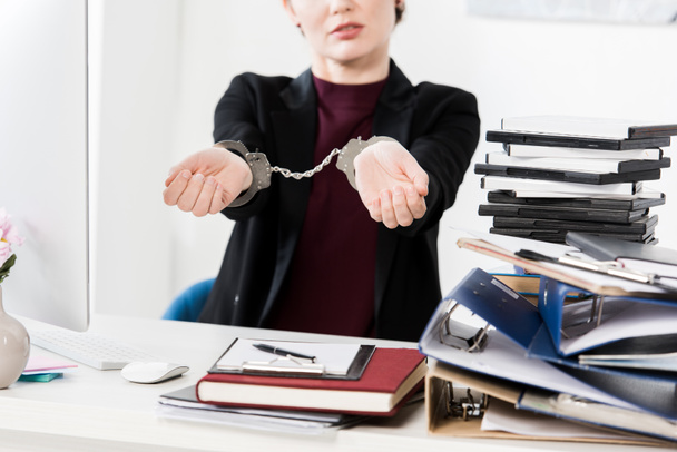cropped image of businesswoman showing hands with handcuffs in office - Foto, afbeelding
