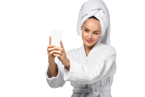 attractive girl in bathrobe with towel on head taking selfie isolated on white - Foto, Imagem