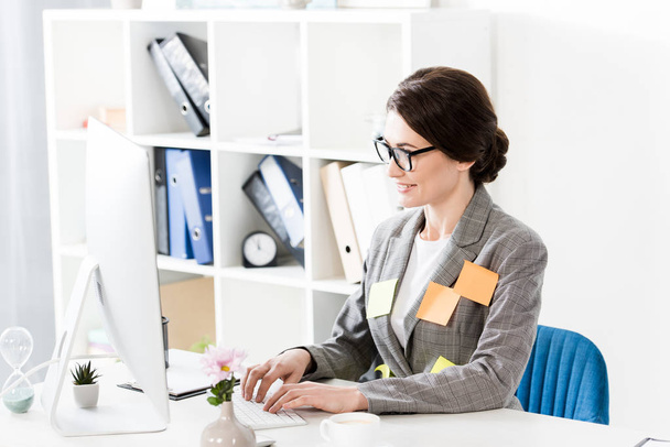 attractive businesswoman with paper stickers on jacket using computer in office - Foto, Imagen