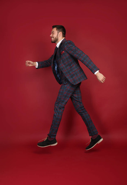 Jumping fashionable man in stylish suit on color background - Фото, зображення