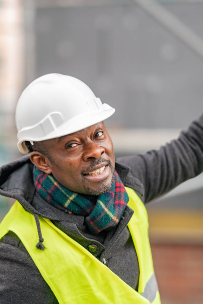 African American engineer wearing yellow protective workwear looking upwards among scaffolding - Photo, Image