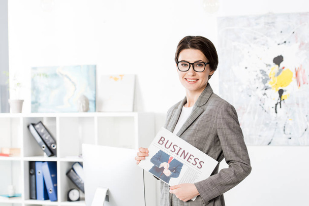 attraktive Geschäftsfrau mit Zeitung im Büro und Blick in die Kamera - Foto, Bild