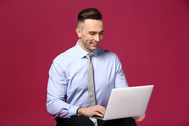 Молодой бизнесмен с ноутбуком на цветном фоне - Фото, изображение