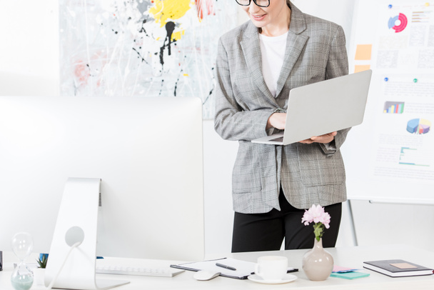 cropped image of smiling businesswoman holding laptop in office - Foto, Imagen