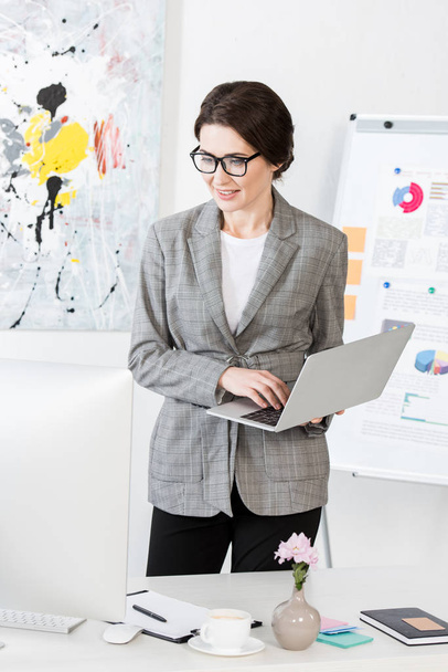 attractive businesswoman holding laptop in office - Foto, afbeelding