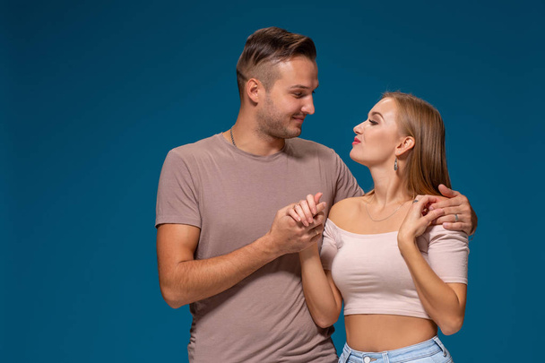 Young couple is hugging on blue background in studio. They wear T-shirts, jeans and smile. - Valokuva, kuva