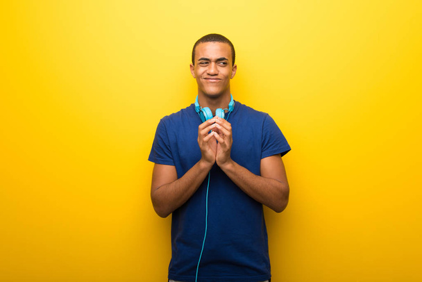 African american man met blauw t-shirt op gele achtergrond gekonkel iets - Foto, afbeelding