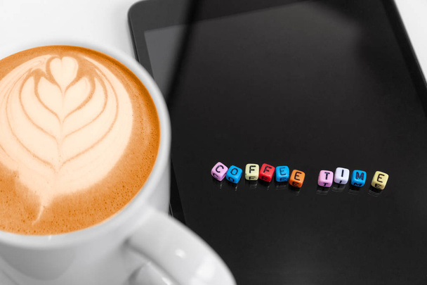 Closeup, Selective focus at the letters cube blocks with coffee time concepts on tablet screen and hot coffee froth art drink in foreground with copy space. - Foto, immagini