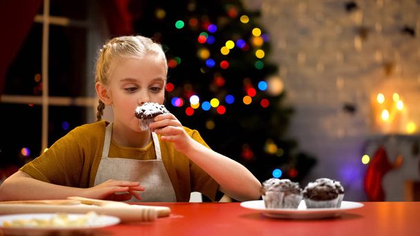 Little girl sniffing chocolate muffin, cozy Christmas mood, holiday atmosphere - Photo, image