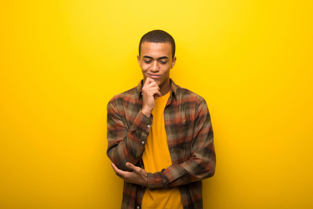 Jeune homme afro-américain sur fond jaune vif regardant vers le bas avec la main sur le menton
 - Photo, image