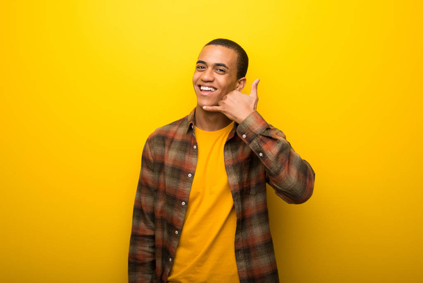 Afro-amerikai fiatalember a telefon gesztus élénk sárga háttérrel. Hívj vissza jele - Fotó, kép