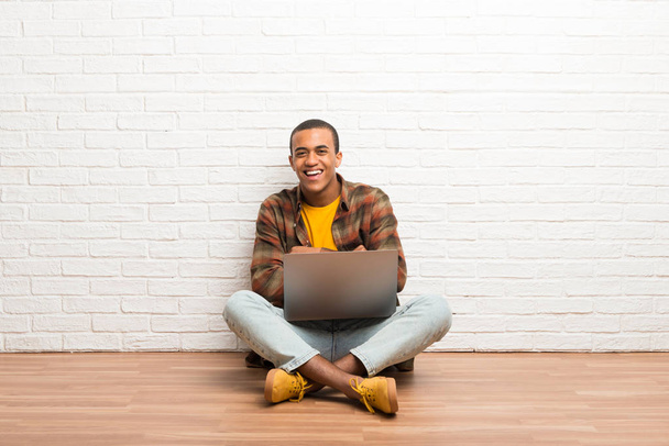 Afrikai amerikai férfi ült a földön az ő laptop, megtartva a karokat, miközben mosolyogva keresztbe - Fotó, kép