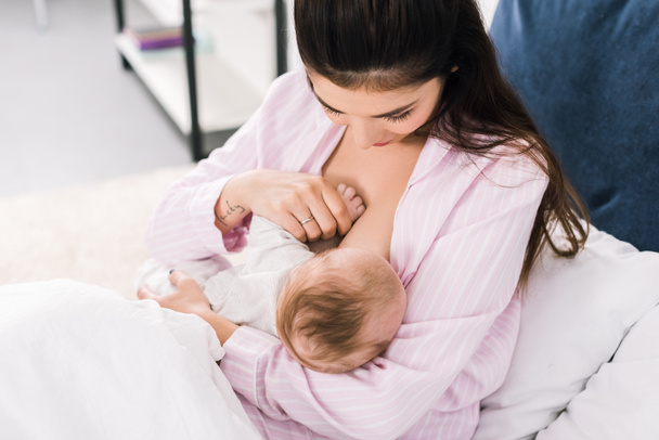 Portret van de jonge moeder borstvoeding kleine baby op bed thuis - Foto, afbeelding