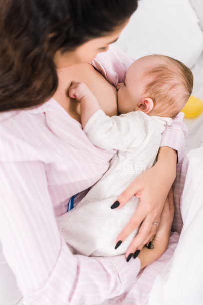 jovem mãe amamentando bebê em casa
 - Foto, Imagem