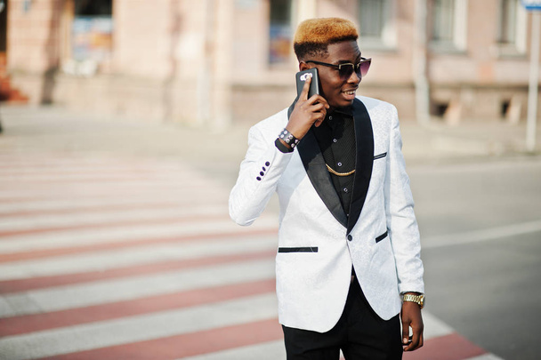 Chic handsome african american man in white suit walking on crosswalk and speaking on phone. - Fotó, kép