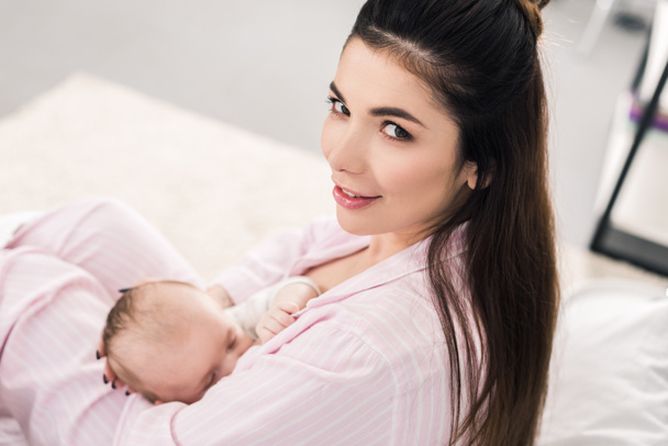 Zijaanzicht van de jonge moeder borstvoeding kleine baby thuis - Foto, afbeelding