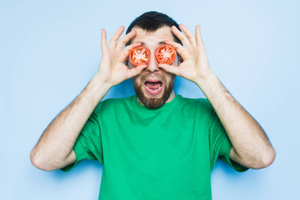 Young bearded man holding slices of red tomatoes in front of his eyes, mouth wide open. Light purple background, copy space. - Photo, Image