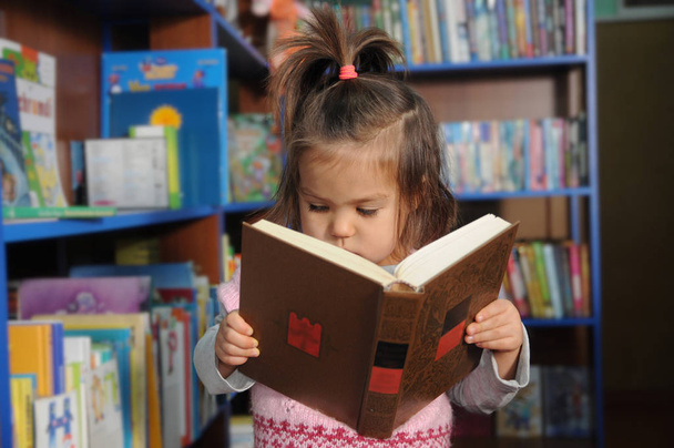 Little girl reading book in library environment - Φωτογραφία, εικόνα