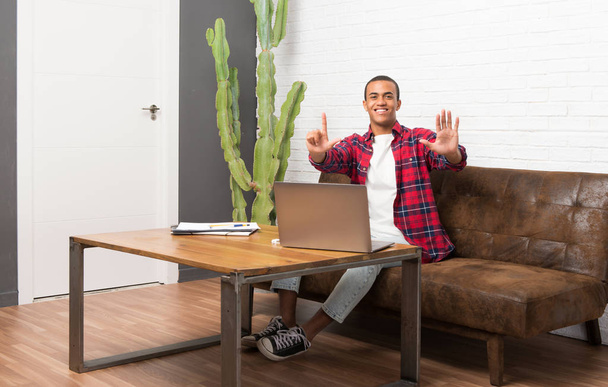 Αφρικανική αμερικανική άνθρωπος με φορητό υπολογιστή στο σαλόνι μετράει επτά με τα δάχτυλα - Φωτογραφία, εικόνα
