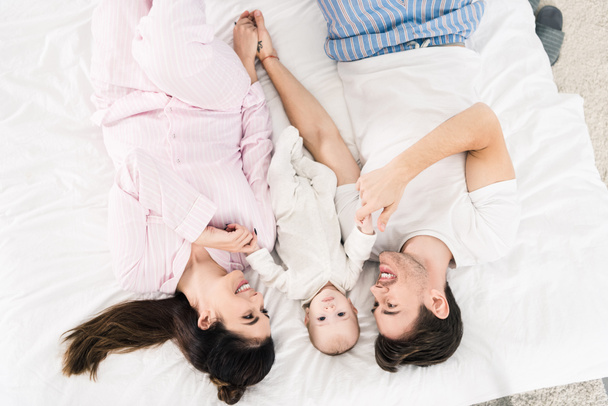 overhead view of happy family with little baby lying on bed together - Foto, imagen