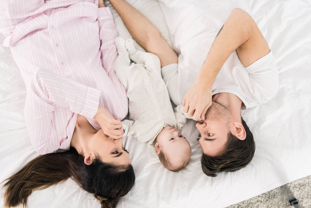 overhead view of happy family with little baby lying on bed together - Fotografie, Obrázek