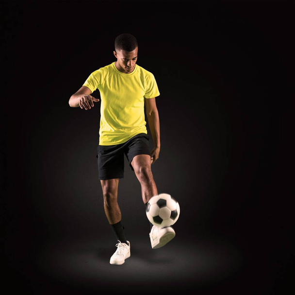 Jogador de futebol homem com pele escura jogando chutando a bola no fundo escuro
 - Foto, Imagem